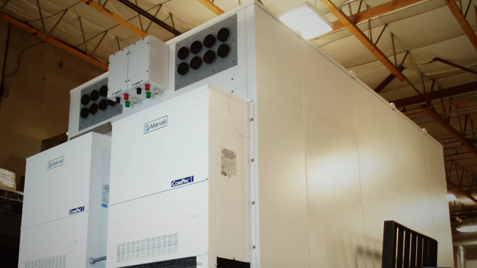A white walk-in telecom shelter with two wall-mounted HVAC units, inside Premier's plant