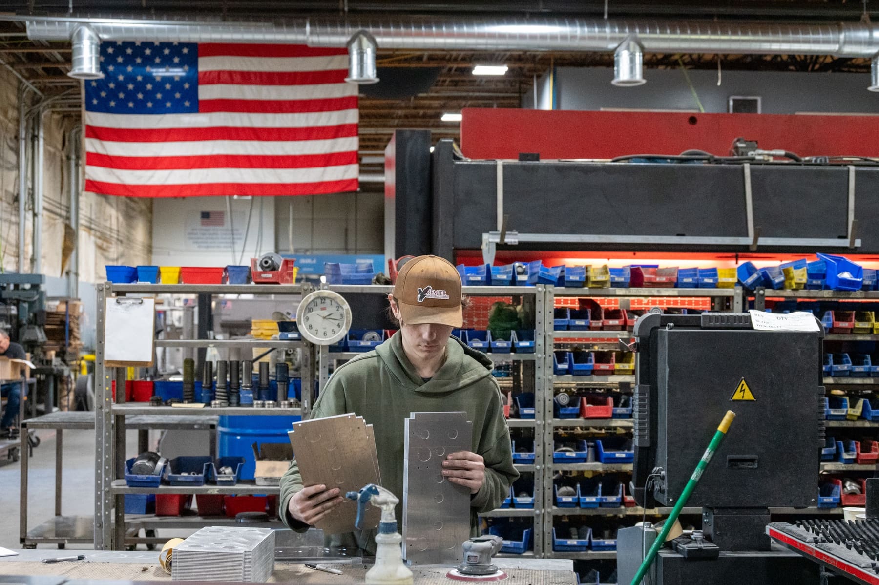 An operator checking a part under the US flag on the shop floor